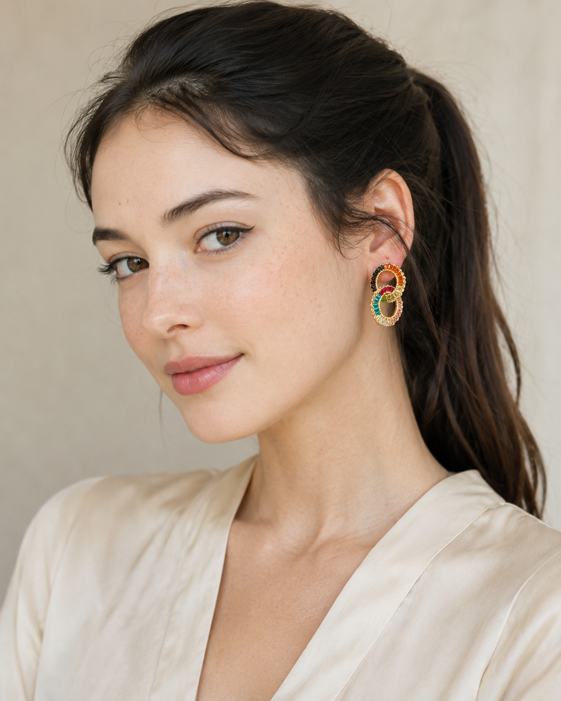 Woman wearing colorful hoop earrings against a neutral background. Handmade in Brazil, these small double link hand crocheted earrings feature 18 karat gold filled wire, multicolor crystals, lightweight comfort, and hypoallergenic nickel free materials.