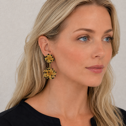 Woman wearing gold earrings with black accents against a neutral background. Hand-crocheted double mandala earrings made with 18 karat gold filled wire and colorful bead accents.