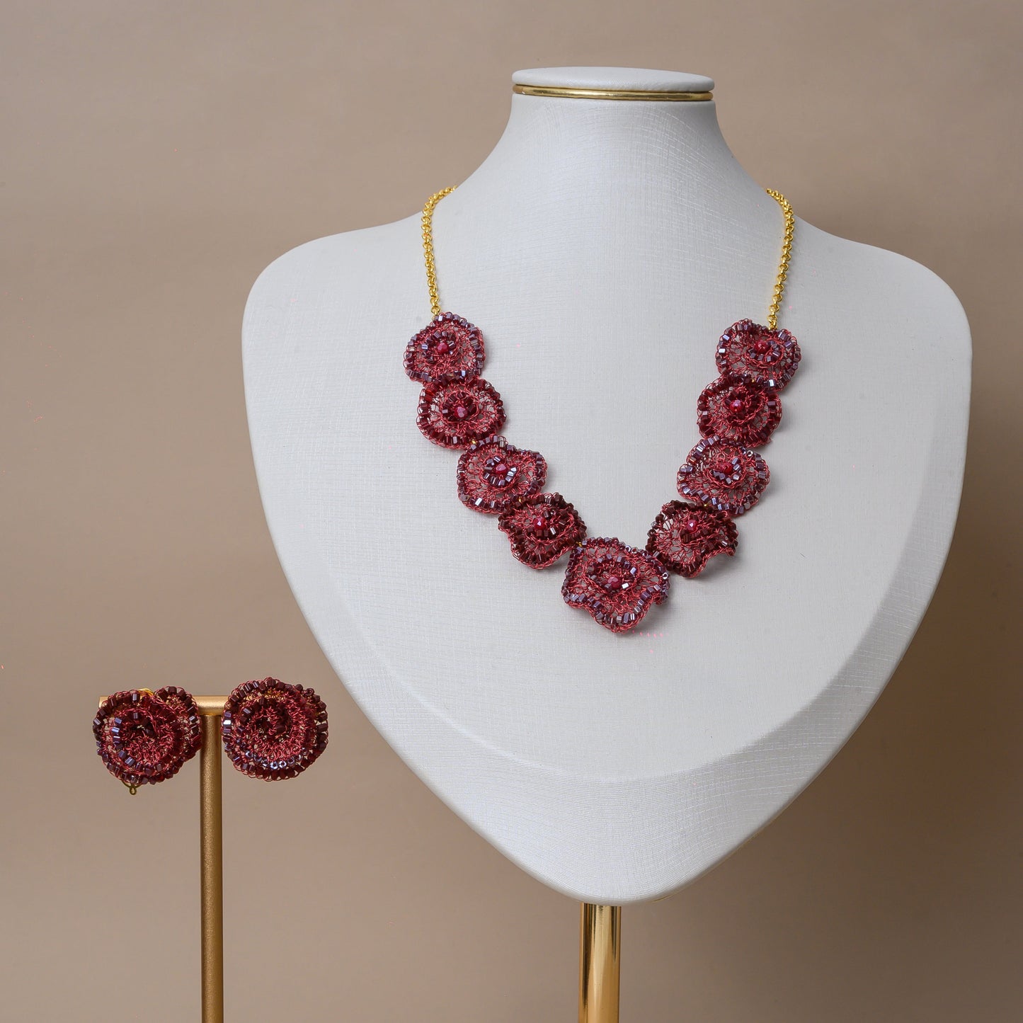 Jewelry set with red floral earrings and necklace on a mannequin bust against a beige background