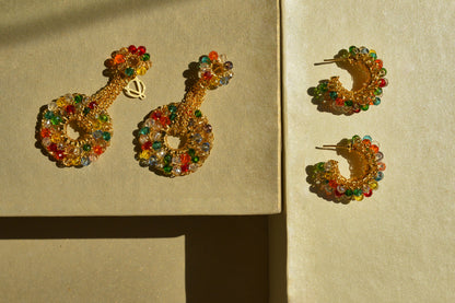Gold hoop earrings with colorful beads on a beige background. Handmade in Brazil, these hand crocheted earrings feature 18 karat gold filled wire, multicolor crystals, lightweight comfort, and hypoallergenic nickel free materials.