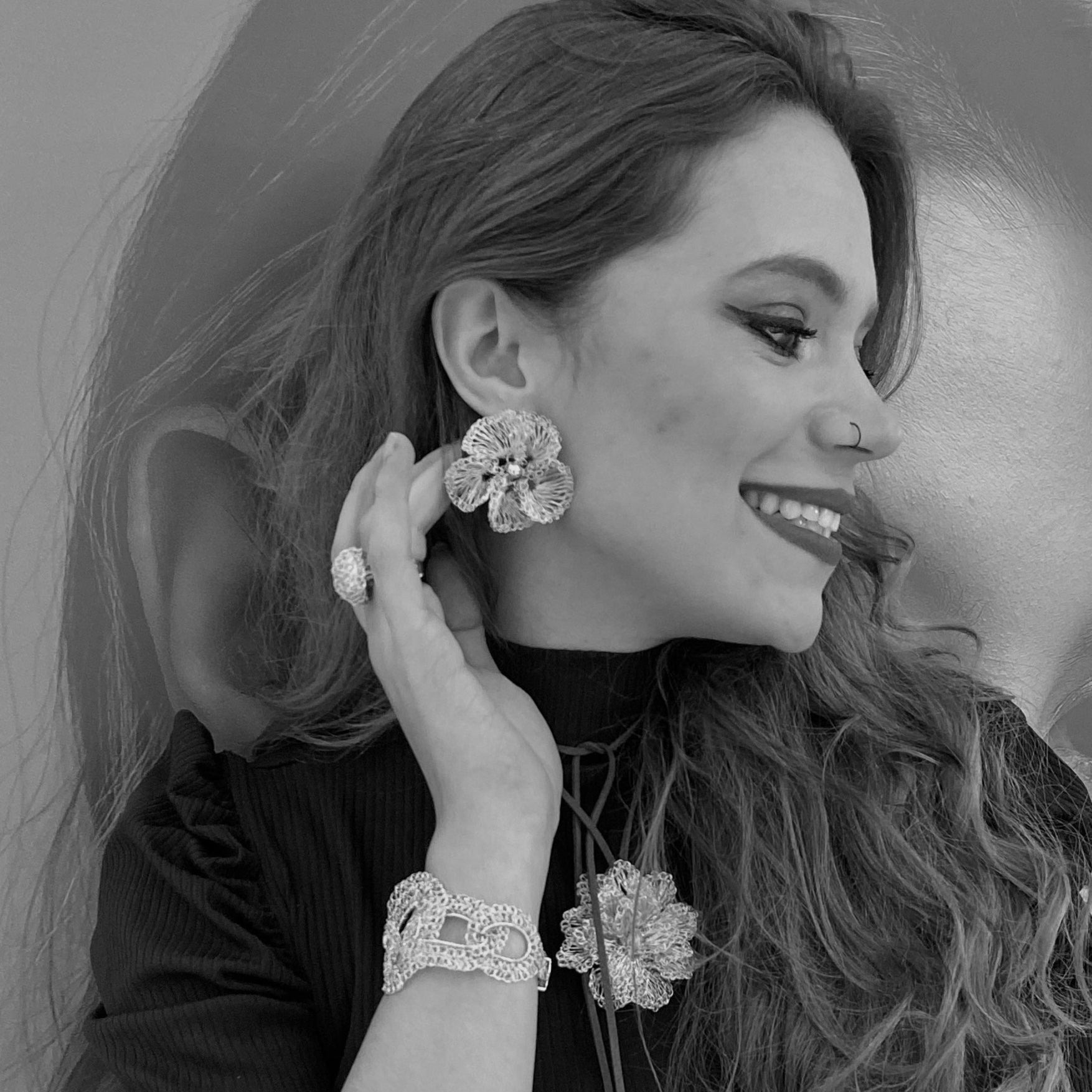Black and white photo of a woman adjusting her earrings with a blurred background