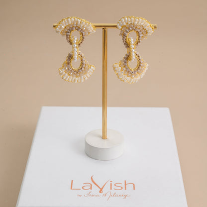 Pair of gold and pearl earrings on a stand with 'LaVish' branding on a beige background