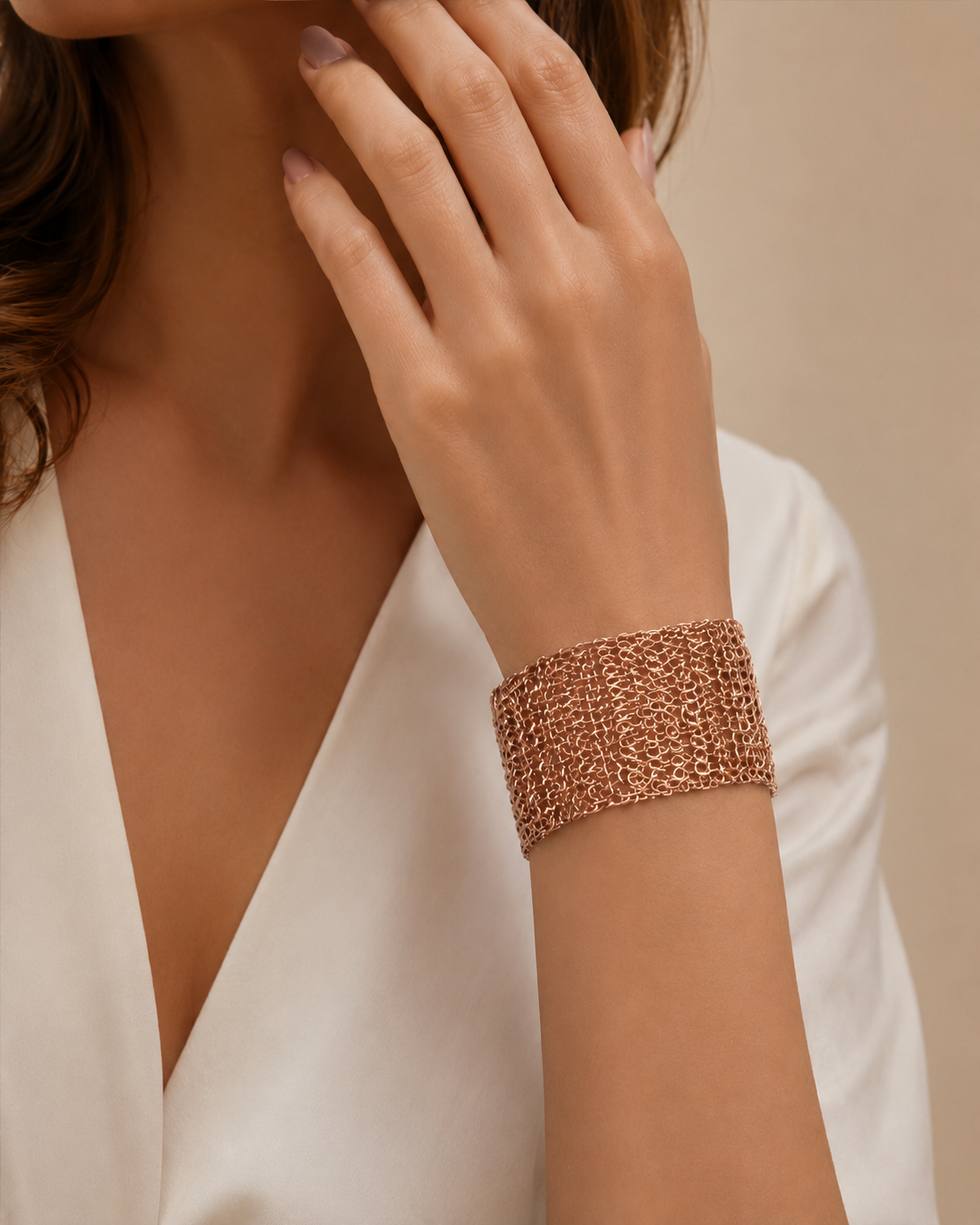 A close-up of a woman's hand and wrist wearing a wide, textured rose gold cuff bracelet, paired with a white V-neck top against a soft beige background. Hand-crocheted rose gold cuff bracelet handmade in Brazil with 18 karat rose gold filled wire, intricate crochet texture, and matching magnetic closures.