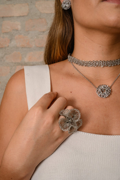 Woman wearing silver jewelry including earrings, necklace, and ring against a brick wall background.