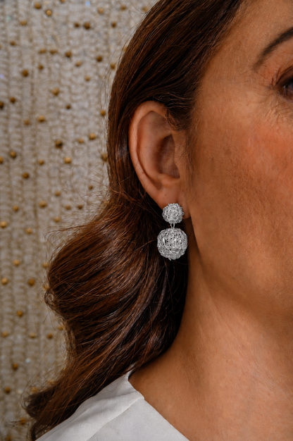 Close-up of a person wearing silver earrings with a textured wall background