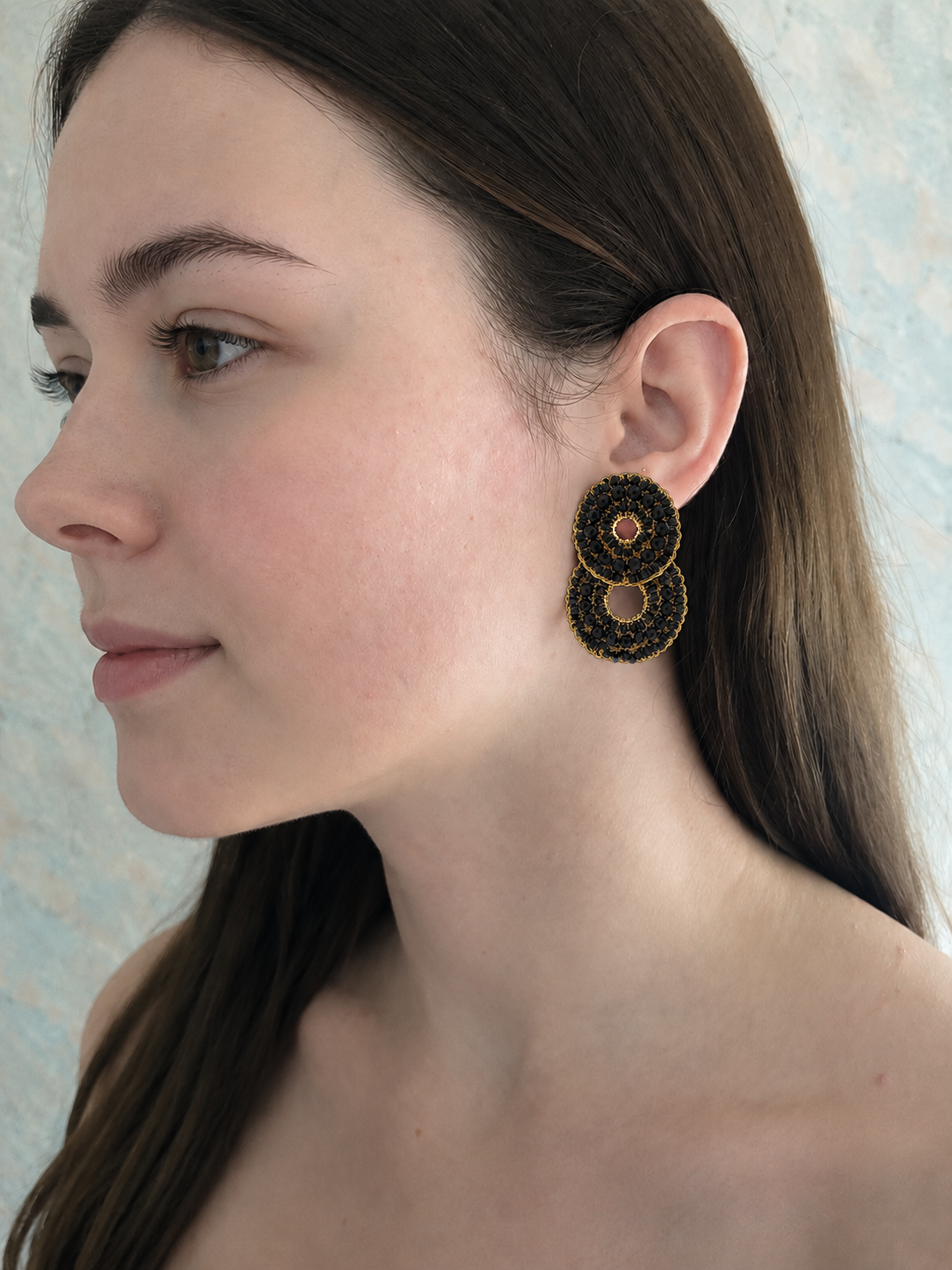Woman wearing a black and gold earring against a neutral background