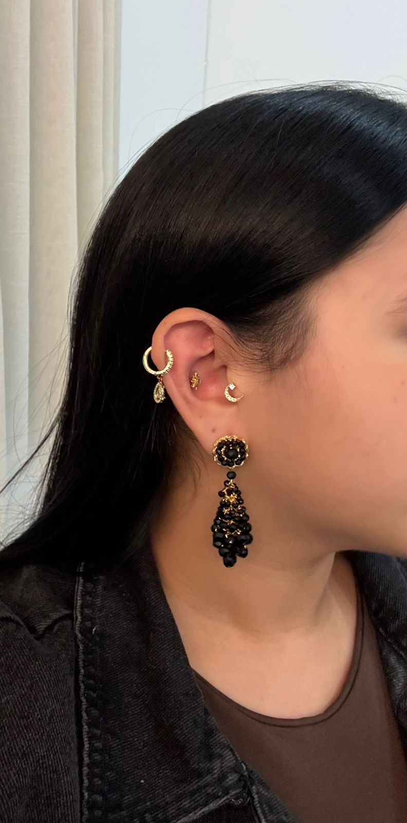 Close-up of a person wearing gold hoop earrings and black dangling earrings.