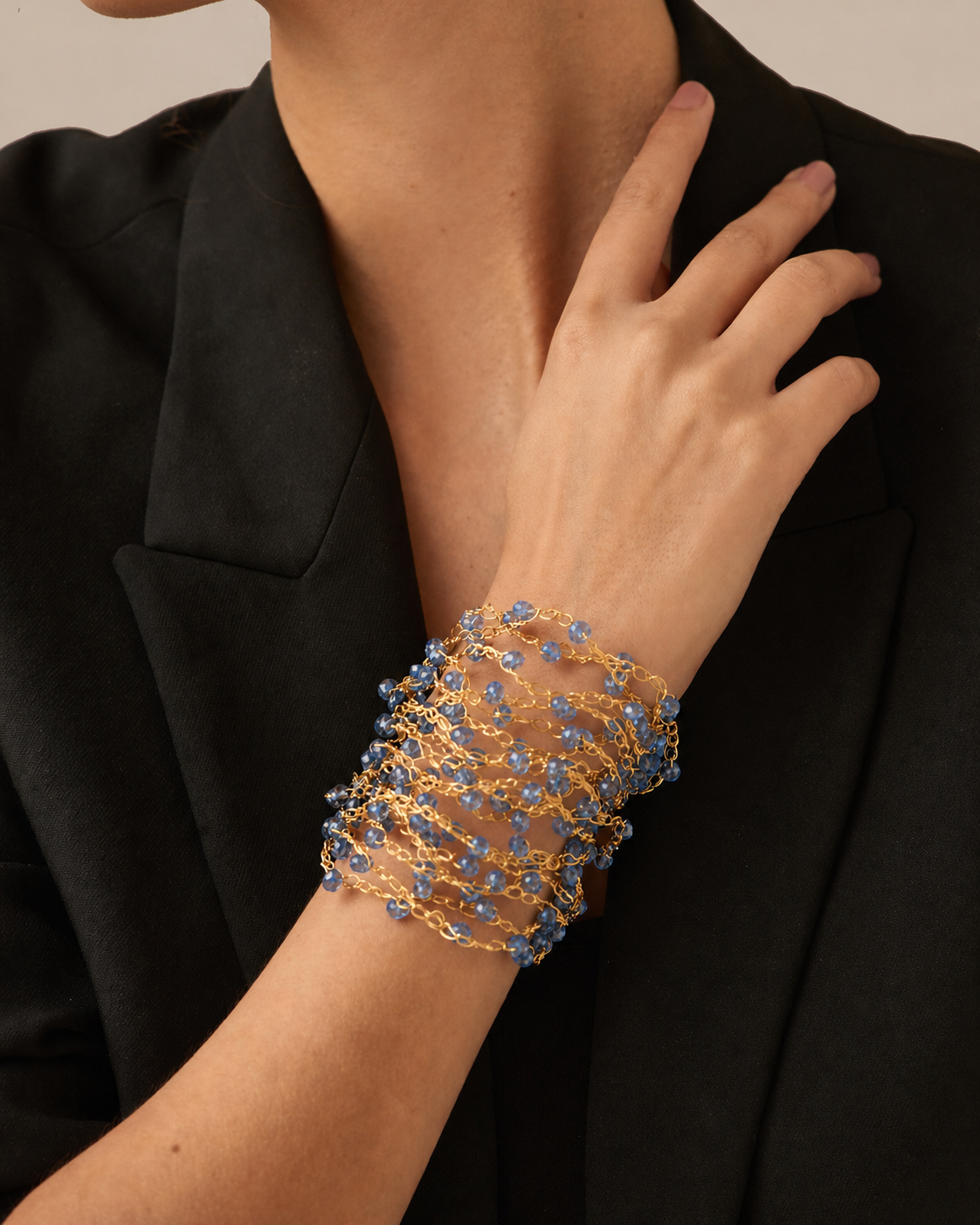 Gold bracelet with blue stones on a person's wrist against a black background. hand-crocheted cuff bracelet, gold cuff bracelet, blue crystal bracelet, 18k gold filled bracelet, handmade Brazilian jewelry, artisan cuff bracelet, lightweight bracelet, hypoallergenic bracelet, nickel free bracelet, magnetic clasp bracelet, resort jewelry, vacation bracelet, evening bracelet, statement cuff bracelet, luxury handmade bracelet