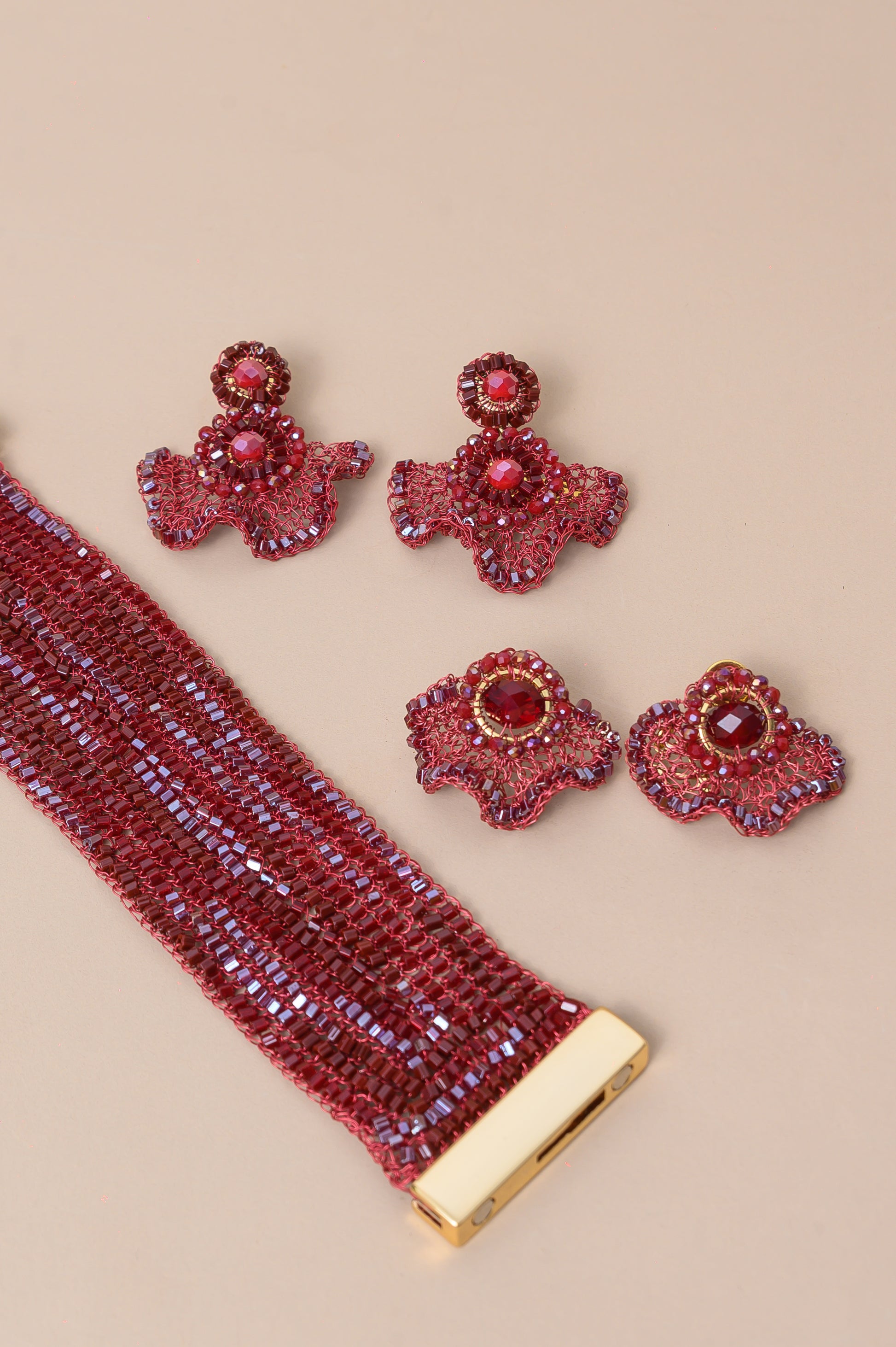 Red gemstone bracelet and earrings on a beige background Burgundy Mix Celosia handmade post earrings with a fan-shaped crochet design, faceted burgundy crystal center and shimmering bead accents.