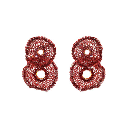 A pair of textured, glittery red earrings shaped like stylized numbers 8, displayed on a clean white background. Shop the Crista Duo Earrings, hand-crocheted in Brazil with rich burgundy tones, shimmering bead accents and a lightweight double-circle design.
