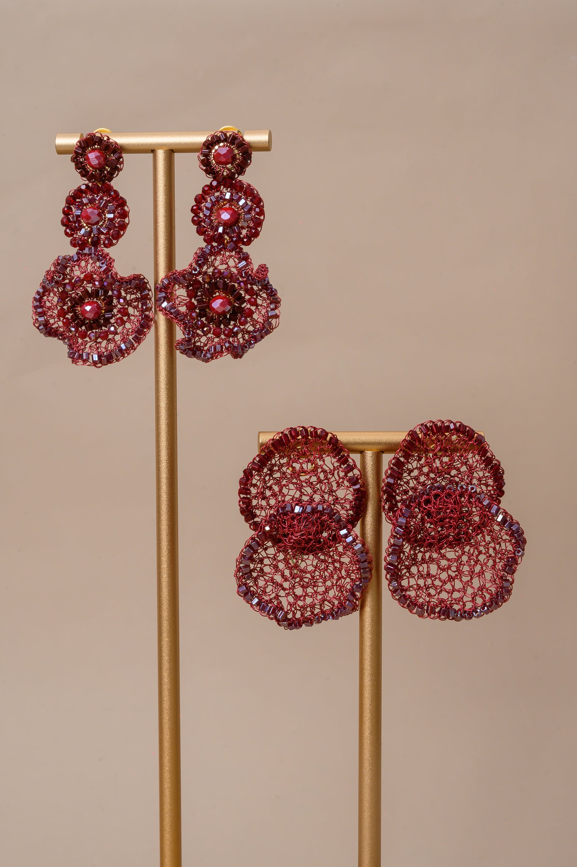 Pair of red floral earrings on a gold stand against a beige background. Shop handmade red statement earrings, hand-crocheted in Brazil with enameled copper wire and sparkling bead accents. Lightweight, hypoallergenic, nickel-free, and perfect for resort, evening, and special occasion styling.