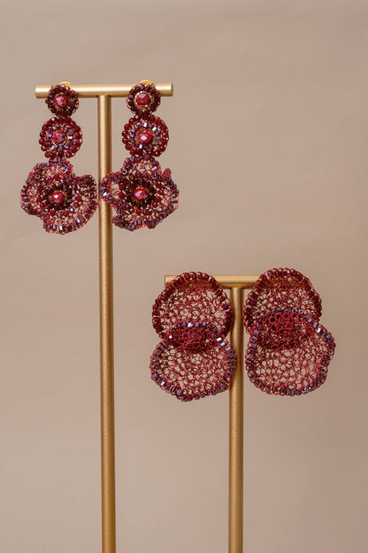 Pair of red floral earrings on a gold stand against a beige background. Shop handmade red statement earrings, hand-crocheted in Brazil with enameled copper wire and sparkling bead accents. Lightweight, hypoallergenic, nickel-free, and perfect for resort, evening, and special occasion styling.