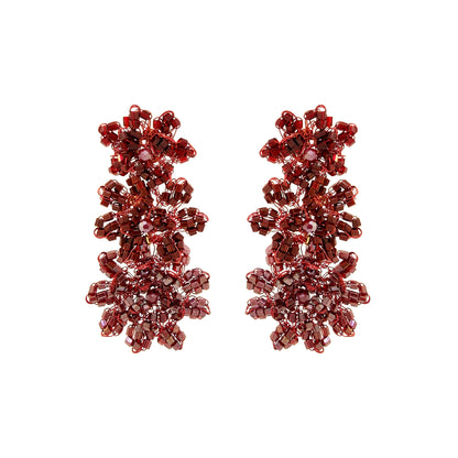 A pair of dangling beaded earrings made of faceted burgundy-red beads arranged in a floral, snowflake-like cluster design, shown on a plain white background. Shop Burgundy Mix Lily Earrings, featuring cascading hand-crocheted flowers with shimmering crystals and beads. Lightweight and handmade in Brazil.