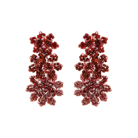 A pair of dangling beaded earrings made of faceted burgundy-red beads arranged in a floral, snowflake-like cluster design, shown on a plain white background. Shop Burgundy Mix Lily Earrings, featuring cascading hand-crocheted flowers with shimmering crystals and beads. Lightweight and handmade in Brazil.