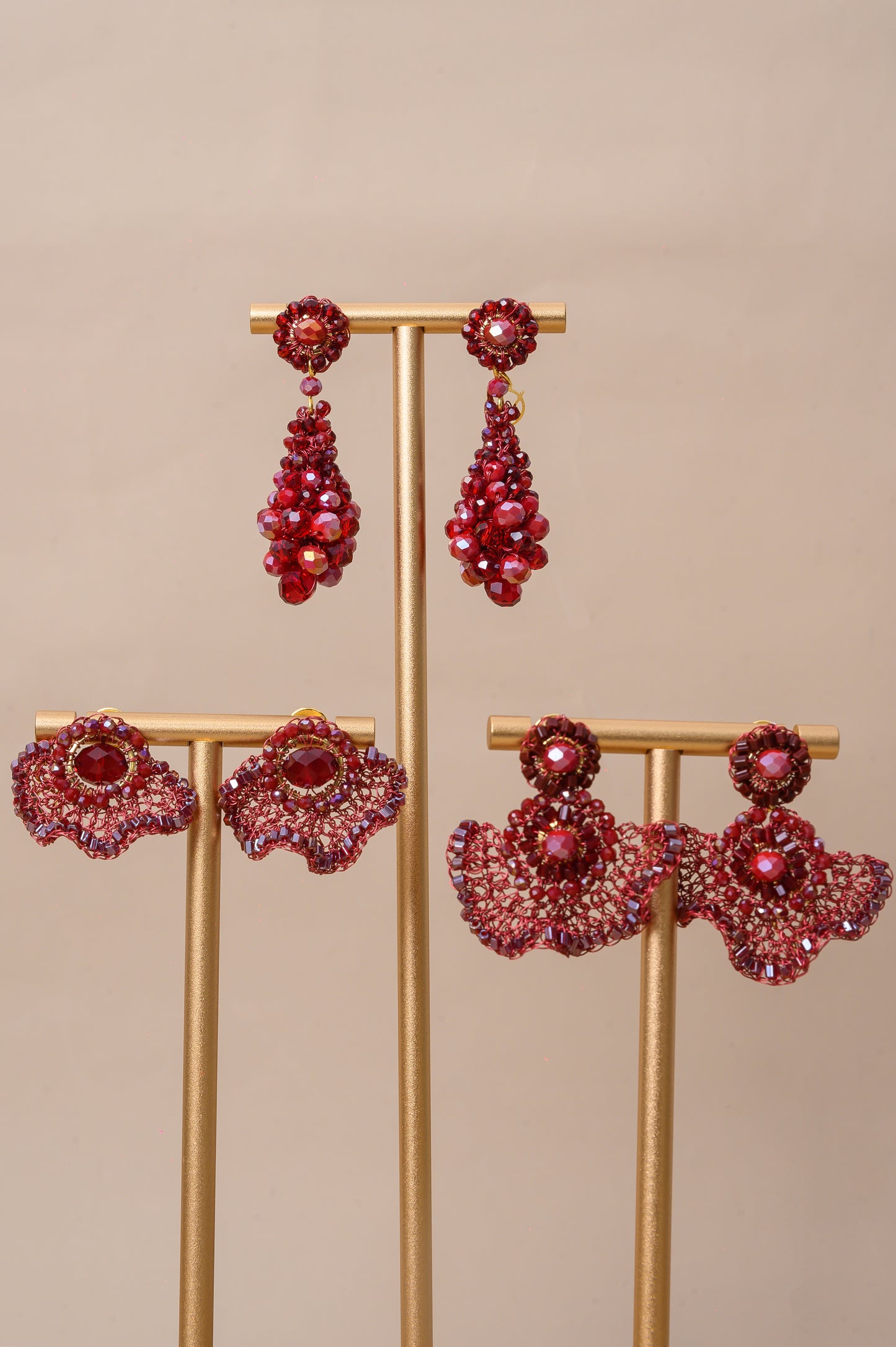 Red gemstone earrings on a gold stand against a beige background