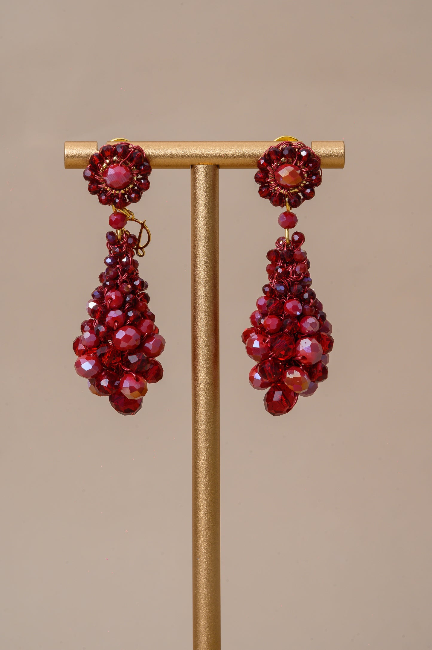Red beaded earrings on a gold stand against a beige background