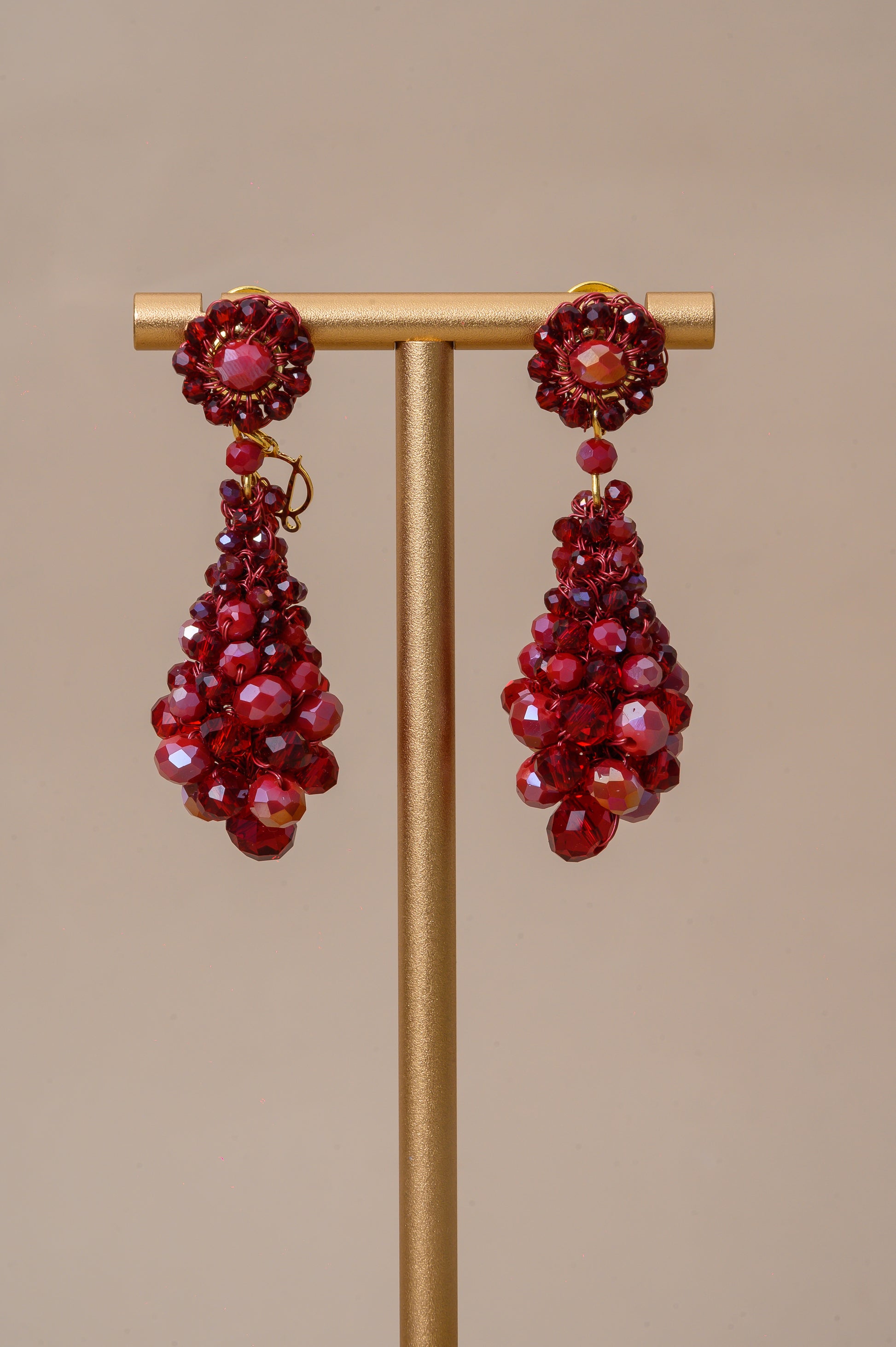 Red beaded earrings on a gold stand against a beige background