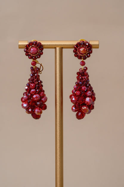 Red beaded earrings on a gold stand against a beige background