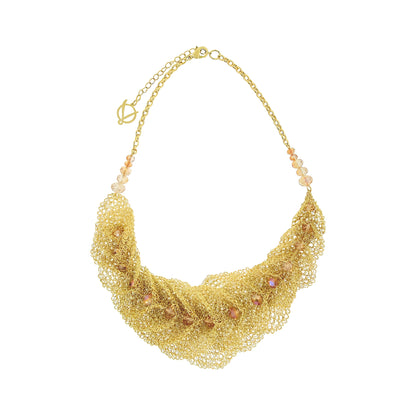 A gold-tone statement necklace featuring a wide, layered mesh bib with small iridescent pink and peach rhinestones, suspended from a delicate gold chain with matching beads. Discover the Cala Embrace Maxi Necklace, handcrafted in Brazil with 18K gold-filled wire, sculptural golden ruffles, and sparkling crystals. Luxury statement jewelry.