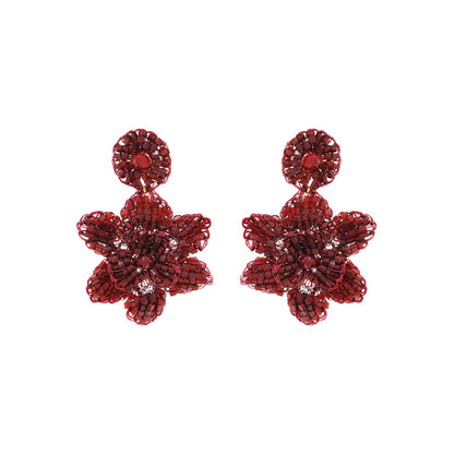 A pair of cherry red, hand-crocheted floral earrings made with enameled copper wire, displayed against a white background. Mini floral hand-crocheted dangle earrings handmade in Brazil with shiny enameled wire and deep cherry red bead accents.
