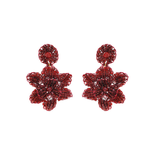 A pair of cherry red, hand-crocheted floral earrings made with enameled copper wire, displayed against a white background. Mini floral hand-crocheted dangle earrings handmade in Brazil with shiny enameled wire and deep cherry red bead accents.