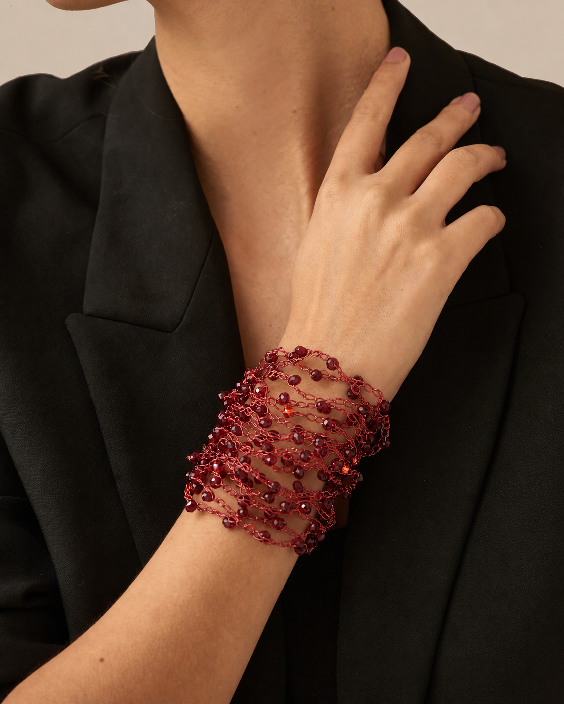 A close-up of a model wearing a wide, multi-layered red beaded mesh cuff bracelet on her wrist, paired with a black blazer. hand-crocheted cuff bracelet, cherry red cuff bracelet, red crystal bracelet, enameled wire bracelet, handmade Brazilian jewelry, artisan cuff bracelet, lightweight bracelet, hypoallergenic bracelet, nickel free bracelet, magnetic clasp bracelet, red statement bracelet, holiday bracelet, evening bracelet, resort jewelry, luxury handmade bracelet