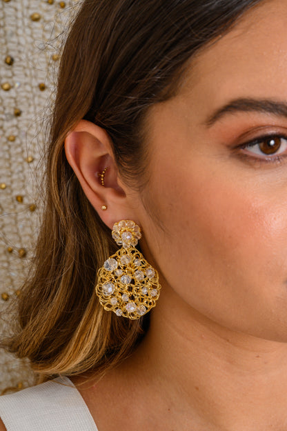 Close-up of a woman wearing gold earrings with a neutral background. Handmade in Brazil, these teardrop mesh earrings feature 18 karat gold filled wire, multicolor crystals, lightweight comfort, and hypoallergenic materials. 