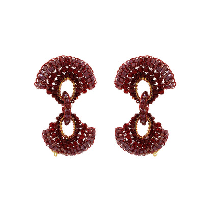 A pair of statement drop earrings crafted from faceted deep red gemstones and accented with gold-tone metal, shown against a plain white background. Red hand-crocheted Duo statement earrings with sparkling bead accents, fan-shaped details and a double-drop silhouette, handmade in Brazil.