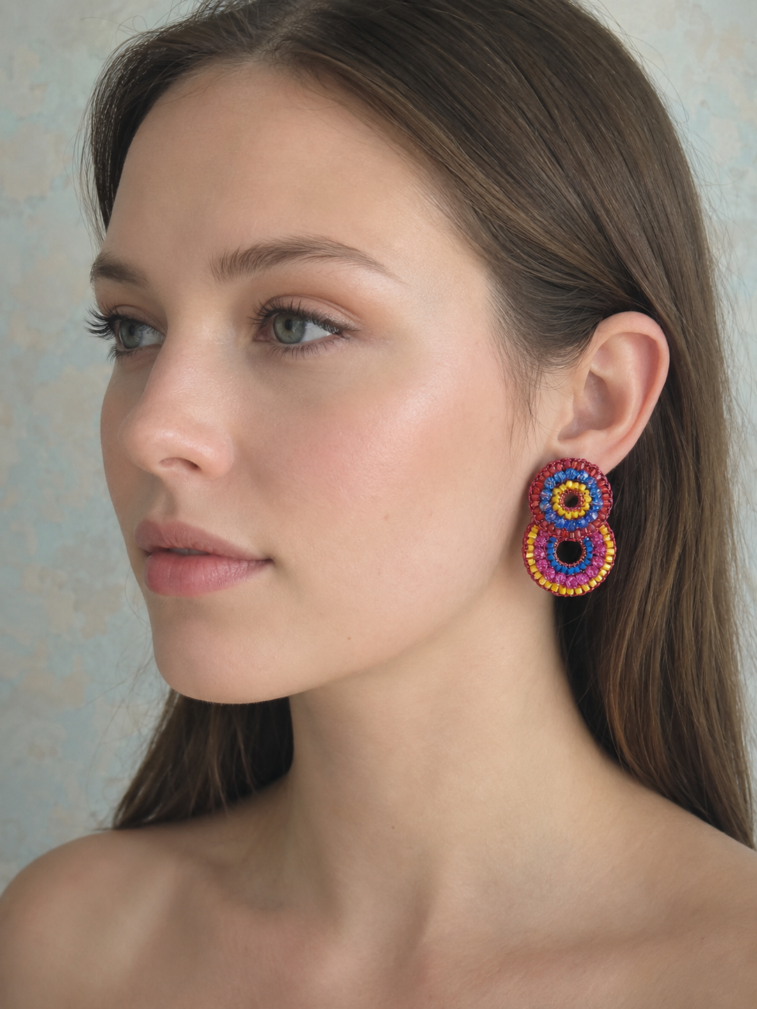 Close-up of a woman wearing colorful beaded earrings against a neutral background