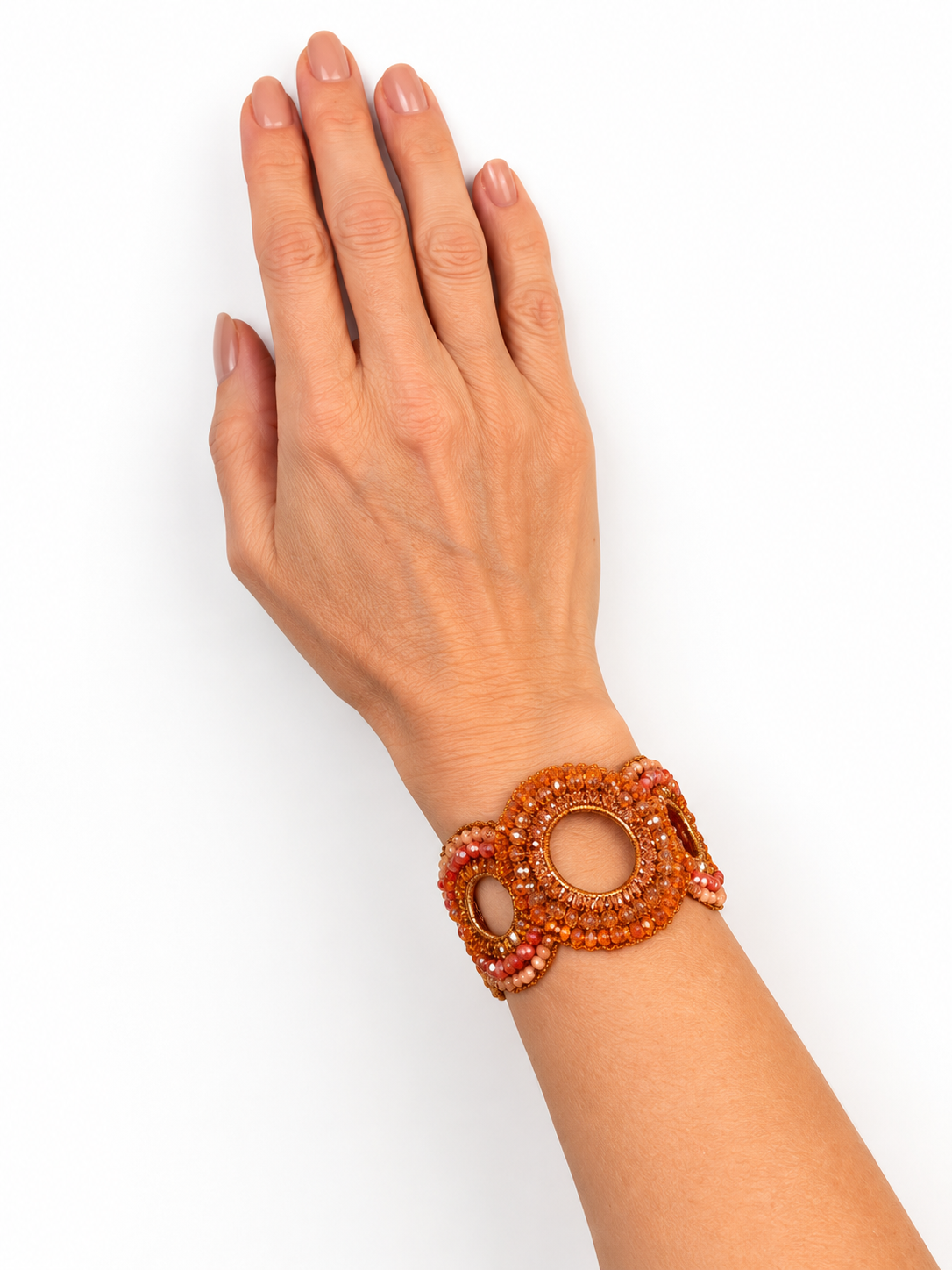 A close-up of a person's hand and wrist wearing a wide, chunky beaded bracelet in orange and pink tones, set against a plain white background. Handmade crochet bracelet, Flamme Mix bracelet, orange crystal bracelet, statement cuff bracelet, Brazilian handmade jewelry, gold-filled bracelet, artisan jewelry, colorful crystal bracelet, Lavish by Tricia Milaneze, Eclosion Collection.