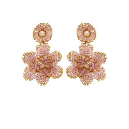 A pair of hand-crocheted earrings with gold and pink detailing, resembling a floral pattern, displayed against a plain background. Floral hand-crocheted dangle earrings handmade in Brazil with 18 karat gold filled wire and delicate mauve bead accents.