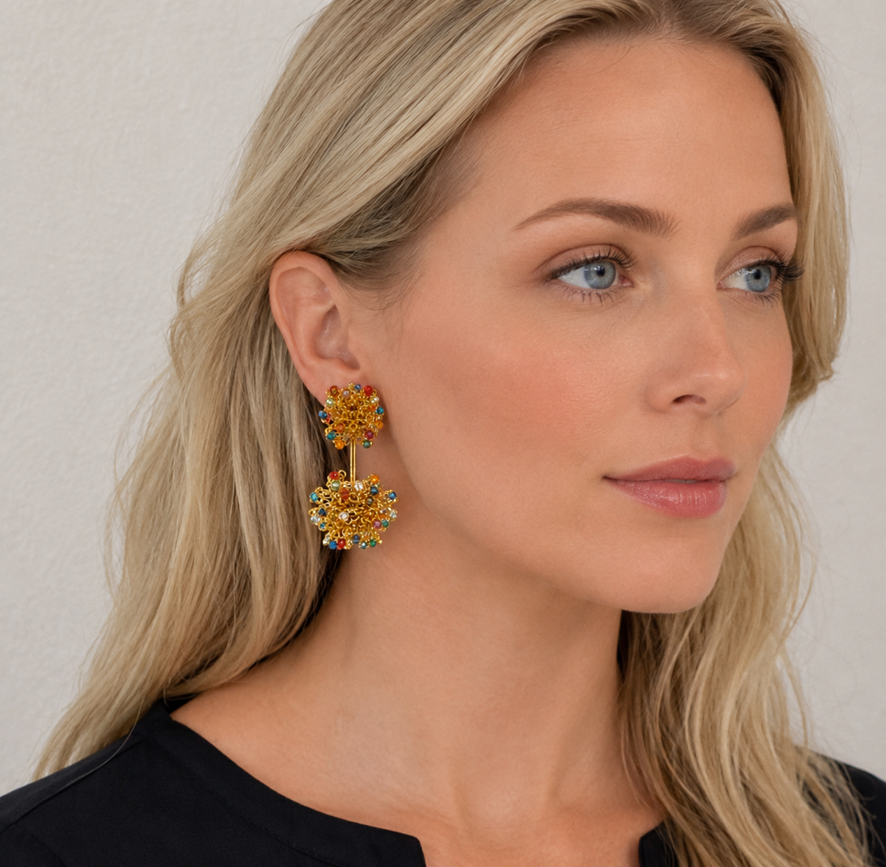 Woman wearing a pair of gold earrings against a neutral background. hand-crocheted earrings, double mandala earrings, handmade Brazilian jewelry, 18 karat gold filled earrings, multicolor bead earrings, lightweight statement earrings, hypoallergenic earrings, nickel-free earrings, artisan earrings, resort jewelry