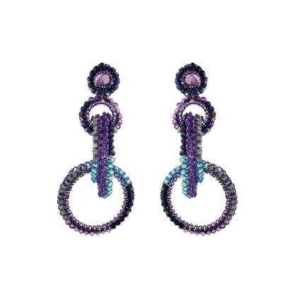 A pair of hand-crocheted earrings with enameled wire and multicolored crystals, displayed against a white background. Interlocked link hand-crocheted earrings handmade in Brazil with rich purple enameled wire, sparkling crystal accents, and teal, lavender, and smoky-toned details.