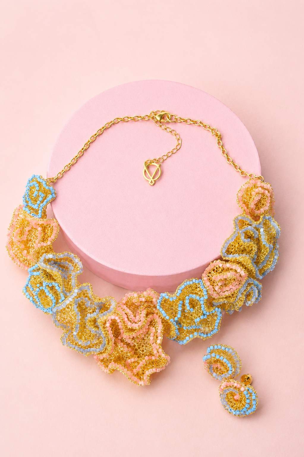 Decorative necklace with floral design on a pink background. Hand-crocheted organic flower cascade necklace made with 18 karat gold-filled wire by Brazilian artisans. Hypoallergenic, nickel-free, and lightweight statement jewelry.