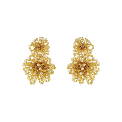A pair of gold-toned statement earrings with intricate floral wirework and small white pearl accents, displayed on a solid white background. Hand-crocheted gold Double Mandala earrings with dimensional floral details and white pearl-like bead accents, handmade in Brazil.