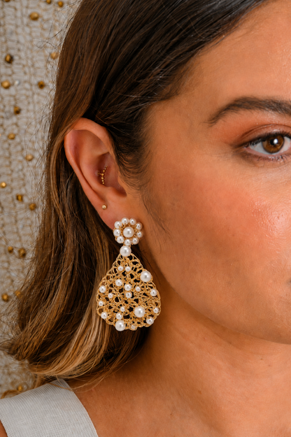 Close-up of a woman wearing gold and pearl earrings with a neutral background. Handmade in Brazil, these teardrop mesh earrings feature 18 karat gold filled wire, multicolor crystals, lightweight comfort, and hypoallergenic materials.