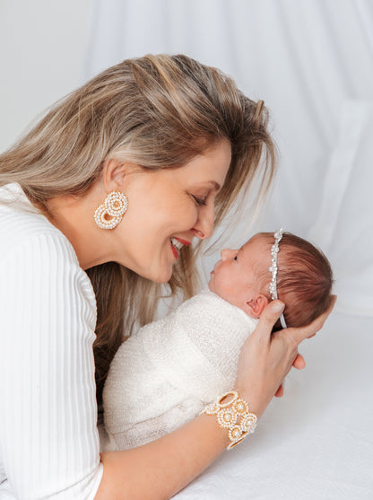 Woman holding a newborn baby against a white background. hand-crocheted double-circle cascade earrings with sparkling crystals and glass beads, handmade in Brazil with enameled copper wire.