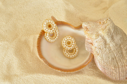 Pair of gold and pearl earrings on a shell with sand background