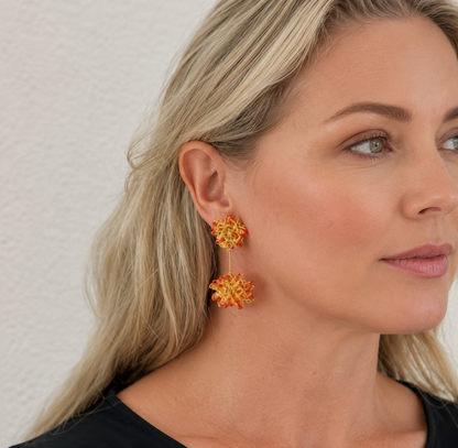 Woman wearing red floral earrings against a neutral background. Hand-crocheted double mandala earrings made with 18 karat gold filled wire and red bead accents