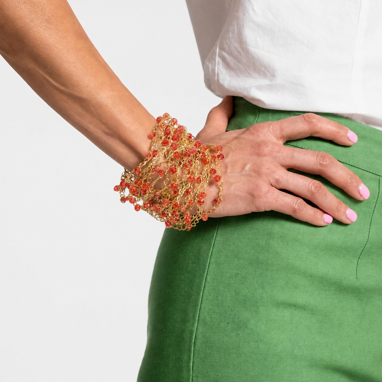 Colorful beaded bracelet on a wrist with a green skirt and white top. hand-crocheted cuff bracelet, gold cuff bracelet, red crystal bracelet, 18k gold filled bracelet, handmade Brazilian jewelry, artisan cuff bracelet, lightweight bracelet, hypoallergenic bracelet, nickel free bracelet, magnetic clasp bracelet, evening bracelet, holiday bracelet, resort jewelry, statement cuff bracelet, luxury handmade bracelet