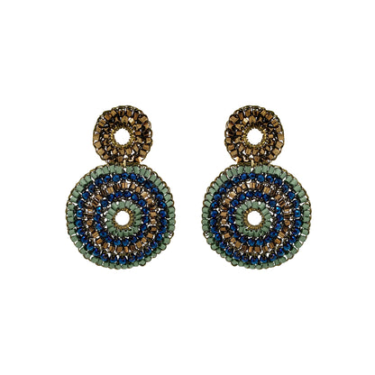 A pair of handmade beaded dangle earrings featuring concentric circular patterns in olive green, navy blue, and metallic gold on a plain white background. Discover Riviera Mix Gia Duo Earrings, hand-crocheted in Brazil with 18K gold-filled wire and shimmering blue, sage green and bronze accents.