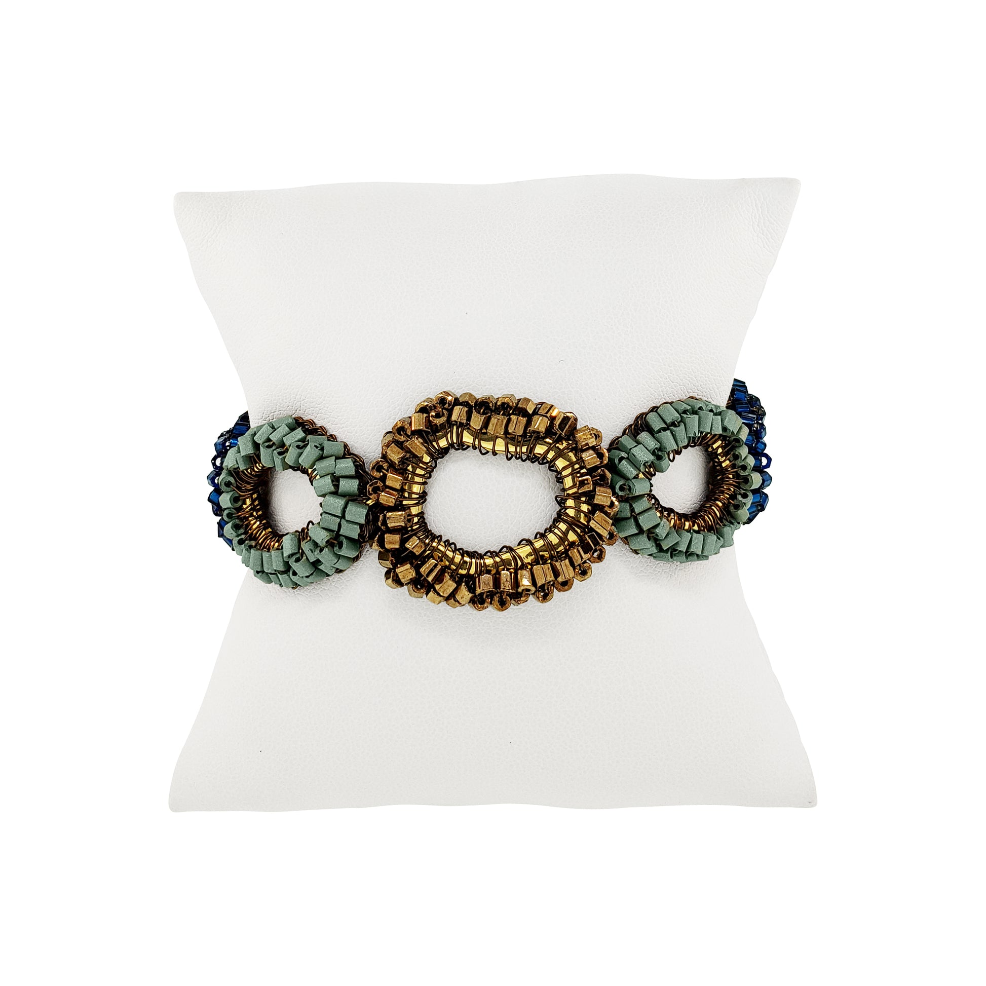 A beaded stretch bracelet with three oval links, featuring a central gold-toned link flanked by sage green and dark blue beaded oval links, displayed on a white mannequin stand.