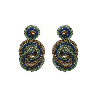 A pair of handmade beaded drop earrings featuring a spiral design in green, blue, and gold, with a small round green and blue top piece on each earring, set against a plain white background. Shop Riviera Mix Loki Earrings, handcrafted in Brazil with 18K gold filled and enameled wire, colorful crystals and intricate crochet detailing.