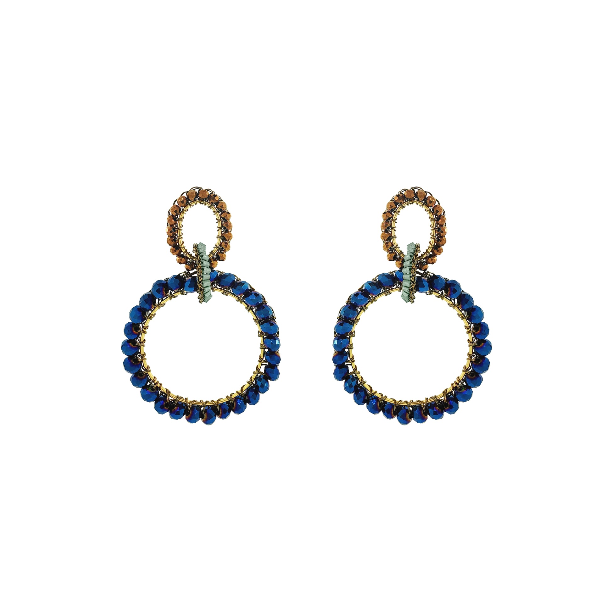 A pair of statement drop earrings featuring large open circular hoops set with deep blue faceted beads and accented with gold-toned metal and small green crystals, shown on a plain white background. Shop Riviera Mix Lola Maxi Earrings, handcrafted in Brazil with 18K gold-filled wire and sparkling blue and bronze crystals in a bold double-hoop design.