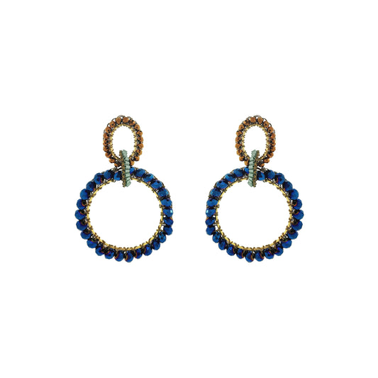 A pair of statement drop earrings featuring large open circular hoops set with deep blue faceted beads and accented with gold-toned metal and small green crystals, shown on a plain white background. Shop Riviera Mix Lola Maxi Earrings, handcrafted in Brazil with 18K gold-filled wire and sparkling blue and bronze crystals in a bold double-hoop design.