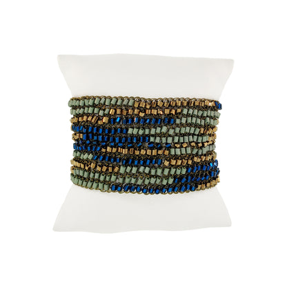 Multicolored beaded bracelet on a white mannequin wrist against a white background. Riviera Mix Signature handmade crochet cuff bracelet with woven deep blue, sage green and bronze accents and gold-tone magnetic clasp.