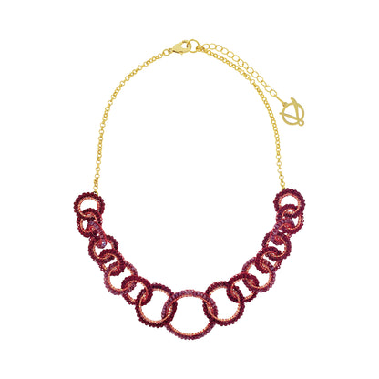 A gold-tone chain necklace featuring a row of interlocking links covered in deep burgundy sequins, presented on a clean white background. Lola handmade statement necklace with interlocking crochet links in burgundy enameled and 18K gold-filled copper wire.
