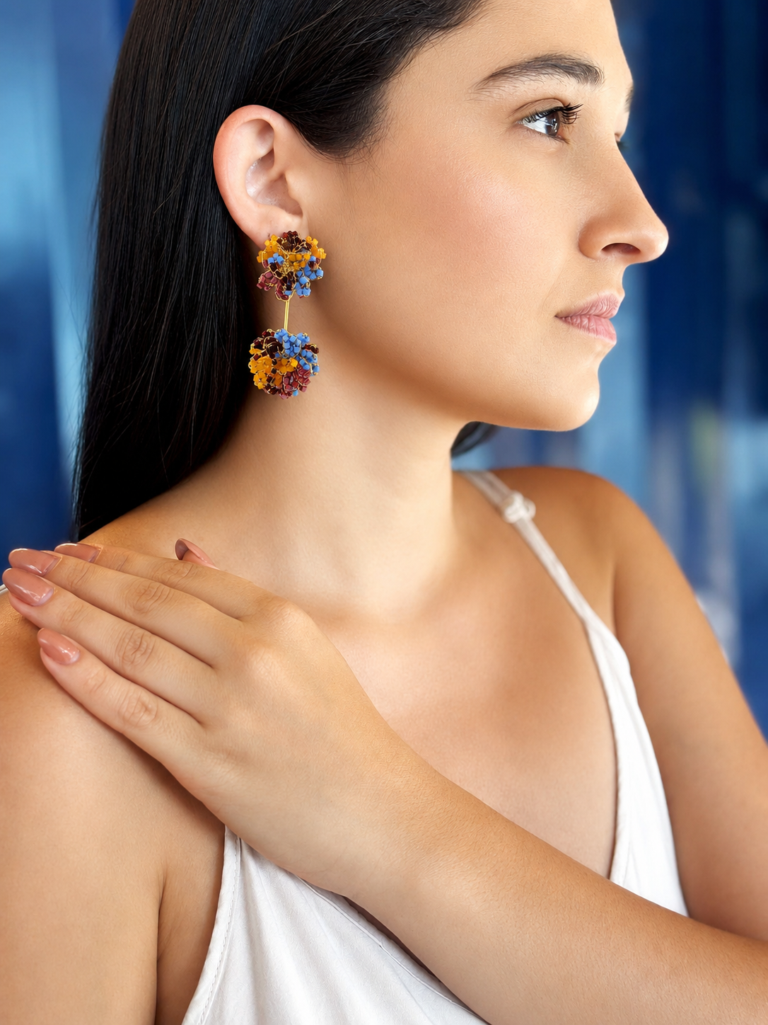 Woman wearing colorful floral earrings with a blue background . Drizzle hand-crocheted dangle earrings made with 18 karat gold filled wire, handcrafted in Brazil with hypoallergenic and nickel-free materials.
