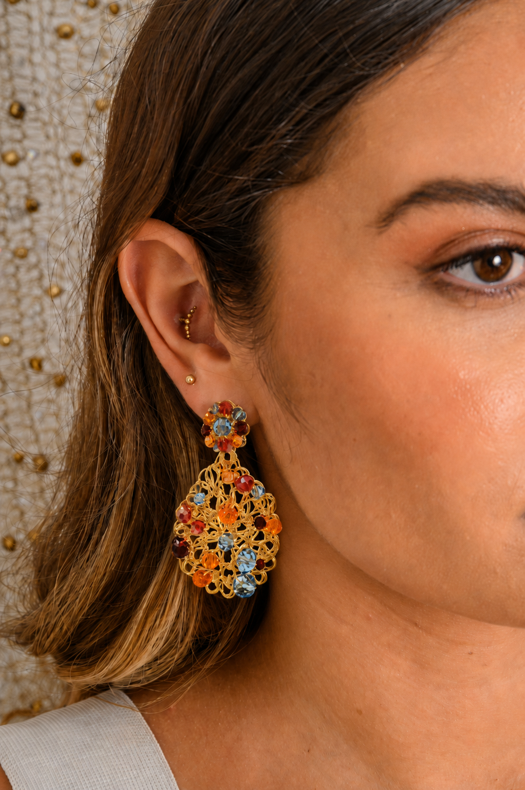Close-up of a woman wearing a colorful floral earring with a textured wall background.