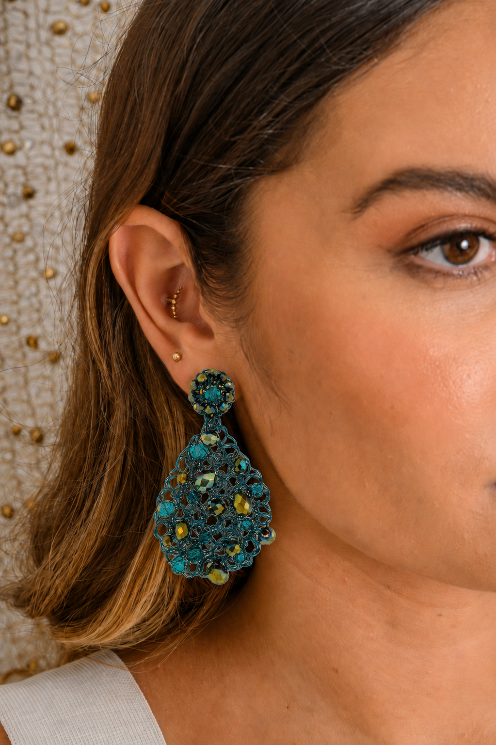 Close-up of a woman wearing a turquoise crocheted earring with a neutral background